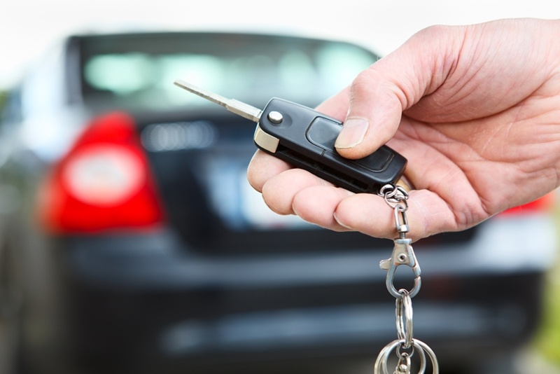 A person's hand is seen holding the keys to a new automobile while the brand new automobile is featured in the background of the picture