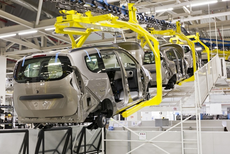 A series of automotive vehicles in the shape of minivans is being carried in the air with robotic arms inside a Mexican automobile manufacturing plant . 